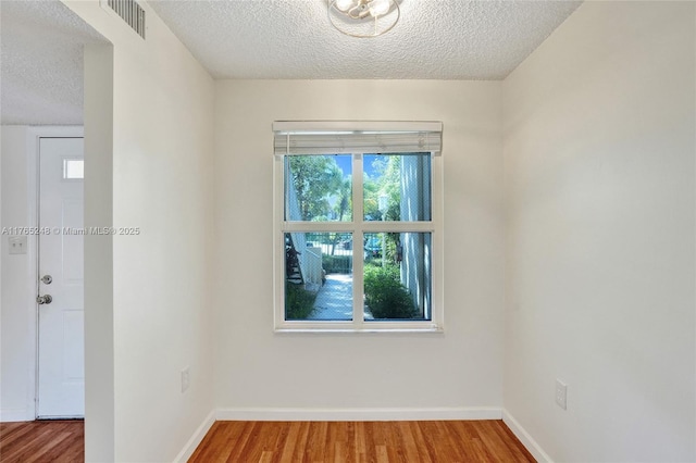 unfurnished room with visible vents, a textured ceiling, baseboards, and wood finished floors