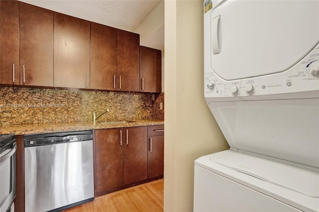 washroom featuring light wood finished floors, stacked washer and dryer, laundry area, a textured ceiling, and a sink