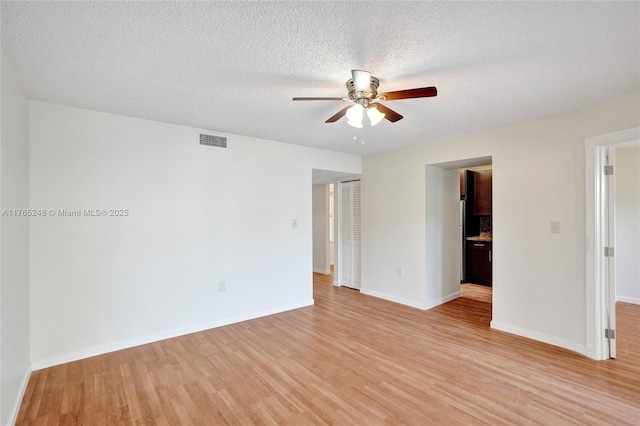 empty room featuring baseboards, visible vents, light wood finished floors, ceiling fan, and a textured ceiling