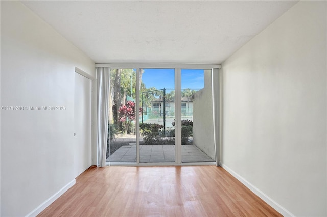 empty room featuring expansive windows, baseboards, and wood finished floors