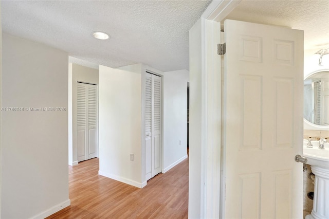 hall with a textured ceiling, baseboards, light wood-style floors, and a sink