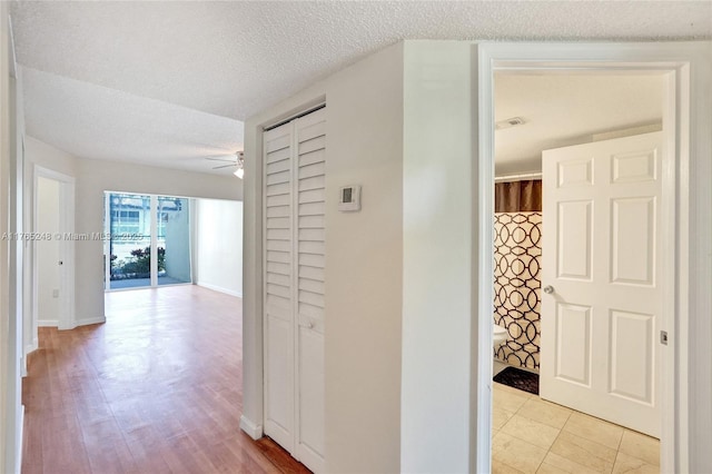 corridor with visible vents, baseboards, a textured ceiling, and light wood finished floors