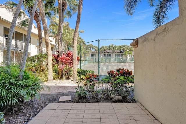 view of patio featuring a tennis court and fence