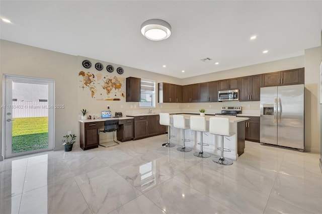 kitchen featuring stainless steel appliances, dark brown cabinetry, a breakfast bar, and light countertops
