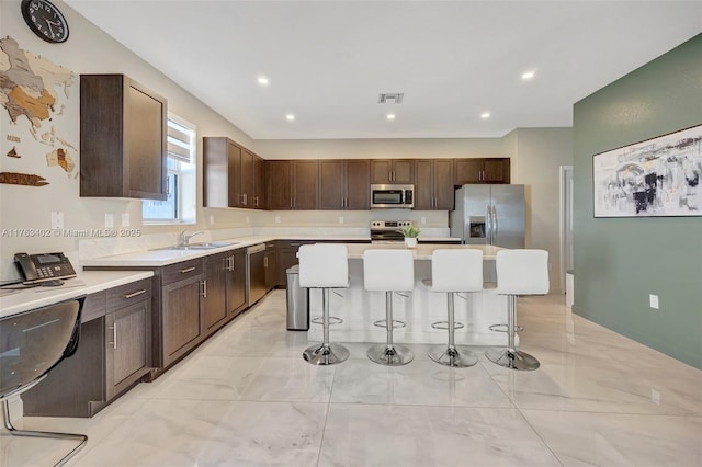 kitchen featuring dark brown cabinetry, light countertops, a kitchen bar, appliances with stainless steel finishes, and a sink