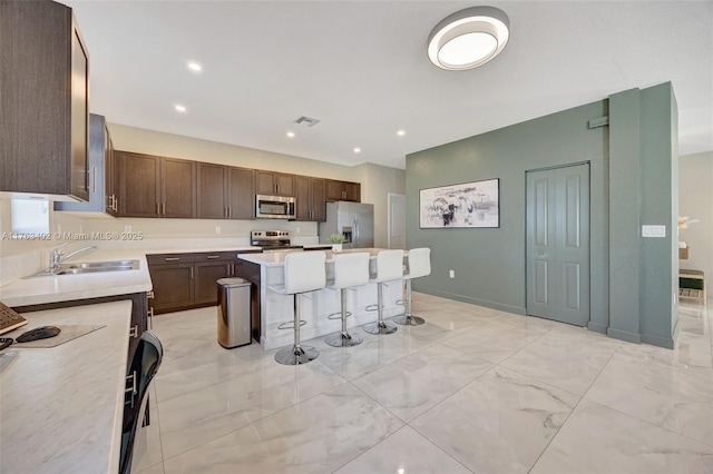 kitchen featuring visible vents, a kitchen island, a breakfast bar, stainless steel appliances, and a sink