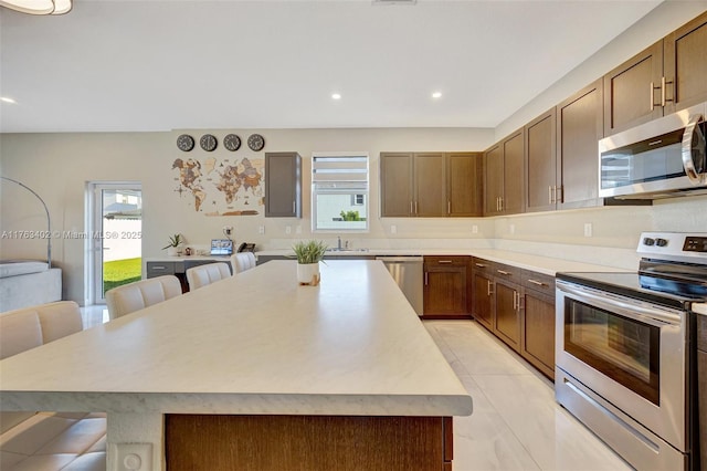 kitchen featuring a kitchen island, a breakfast bar area, light countertops, appliances with stainless steel finishes, and a sink