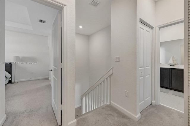 hallway featuring visible vents, carpet floors, baseboards, and an upstairs landing