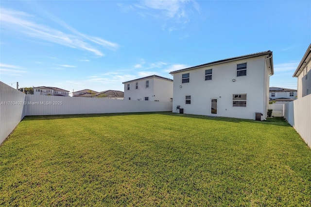 back of house with a fenced backyard, stucco siding, and a yard