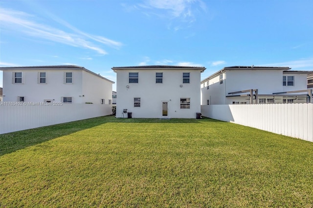 rear view of property with stucco siding, a yard, and fence