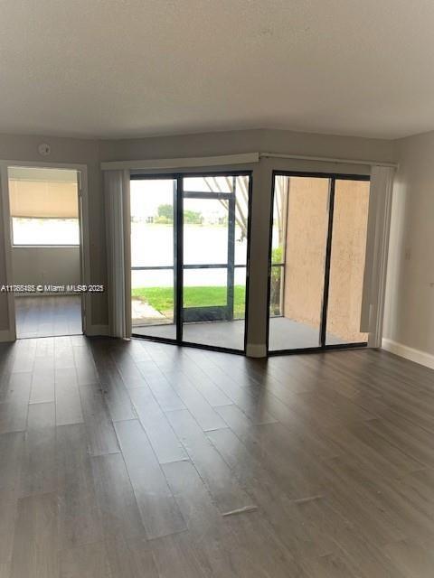 spare room with a textured ceiling, dark wood-type flooring, and baseboards