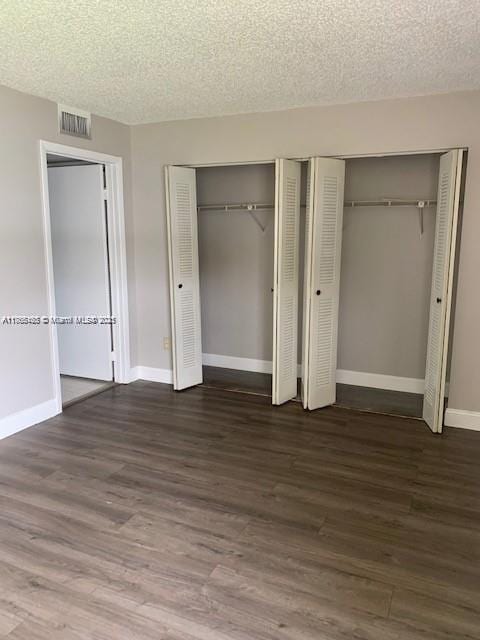 unfurnished bedroom with wood finished floors, visible vents, baseboards, a textured ceiling, and two closets