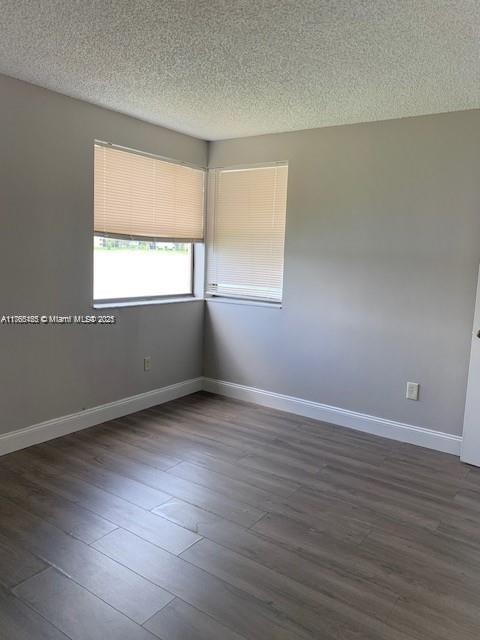 unfurnished room with dark wood-type flooring, baseboards, and a textured ceiling