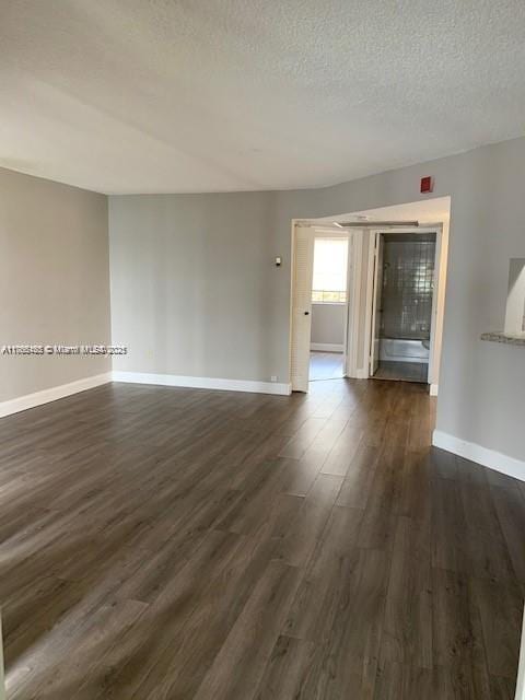 empty room with dark wood-type flooring, baseboards, and a textured ceiling