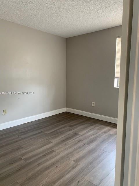 unfurnished room featuring dark wood finished floors, a textured ceiling, and baseboards