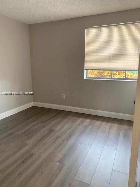 unfurnished room with baseboards, dark wood-type flooring, and a textured ceiling