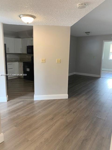 unfurnished room with baseboards, a textured ceiling, and wood finished floors