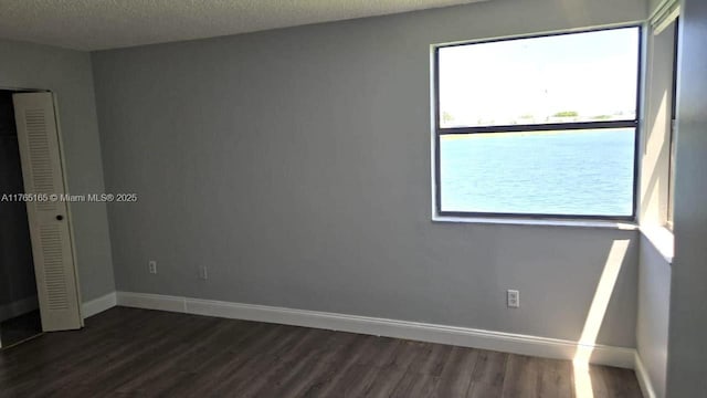 unfurnished bedroom with a closet, a textured ceiling, dark wood-type flooring, and baseboards