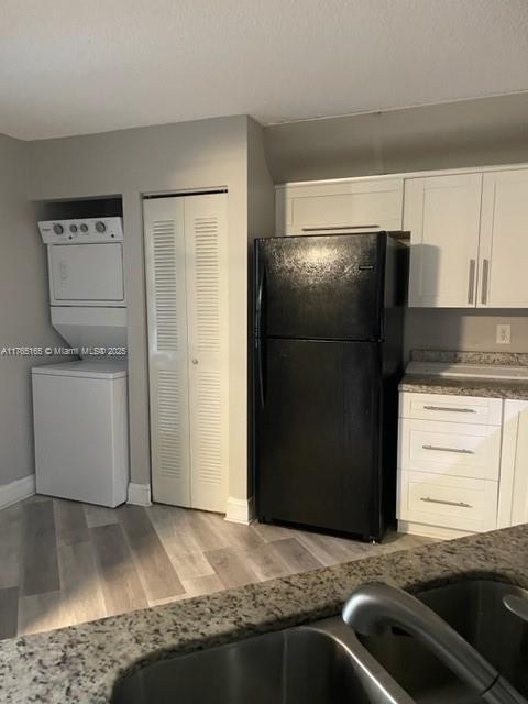kitchen with stacked washer and dryer, light wood-style flooring, white cabinetry, freestanding refrigerator, and baseboards