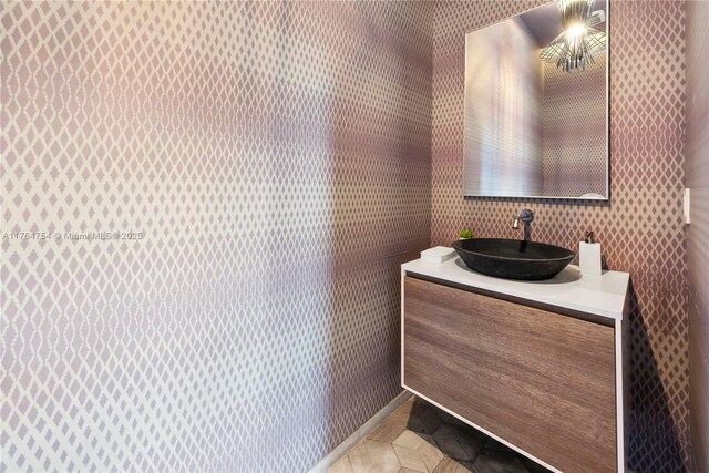 bathroom with baseboards, vanity, and wallpapered walls