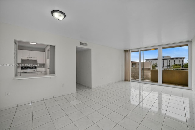 empty room featuring a wall of windows, light tile patterned floors, and visible vents