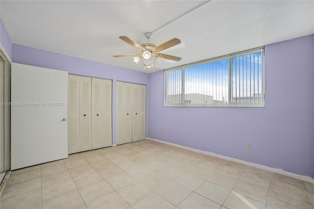 unfurnished bedroom with light tile patterned floors, baseboards, multiple closets, and ceiling fan