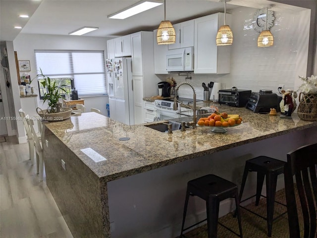 kitchen featuring light wood-type flooring, white appliances, a peninsula, stone countertops, and white cabinetry