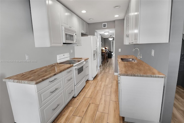kitchen with white appliances, visible vents, wood finish floors, a sink, and white cabinetry