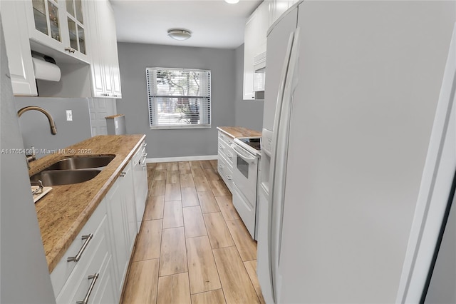 kitchen with wood finish floors, light countertops, white cabinets, white appliances, and a sink