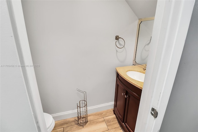 half bath with toilet, vanity, baseboards, and wood finished floors