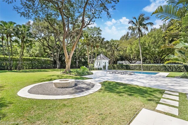 4550 Sunset Dr, Coral Gables, FL 33143 - view of green lawn with a patio area, an outdoor fire pit, an outbuilding, a storage structure, and view of wooded area