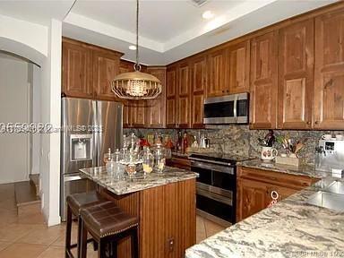 949 Harbor Vw N, Hollywood, FL 33019 - kitchen featuring a center island, stainless steel appliances, arched walkways, light tile patterned flooring, and decorative backsplash
