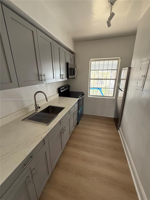 kitchen featuring stainless steel appliances, gray cabinetry, a sink, light wood-style floors, and light stone countertops