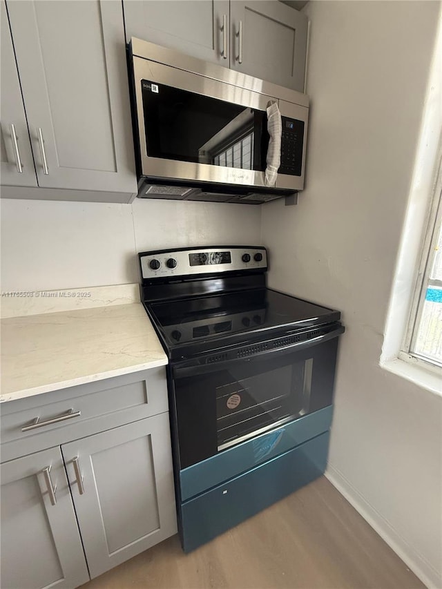 kitchen with electric range oven, gray cabinetry, light wood-type flooring, stainless steel microwave, and baseboards