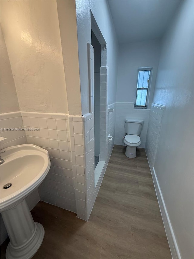 bathroom with a wainscoted wall, toilet, a sink, wood finished floors, and tile walls