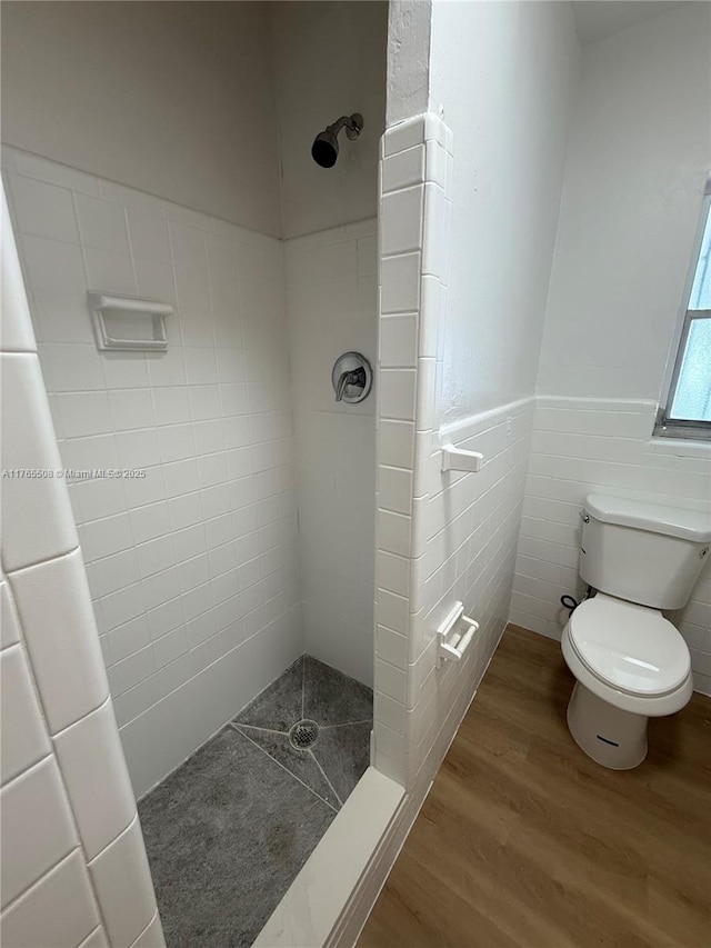 bathroom with wainscoting, toilet, tiled shower, and wood finished floors