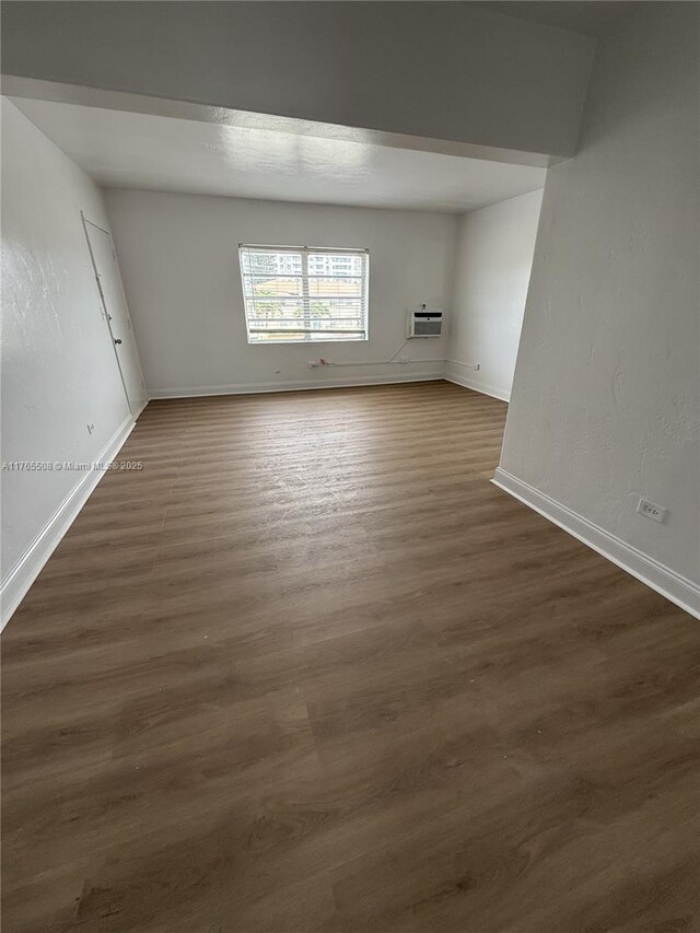 unfurnished room featuring dark wood-type flooring, a wall mounted air conditioner, and baseboards