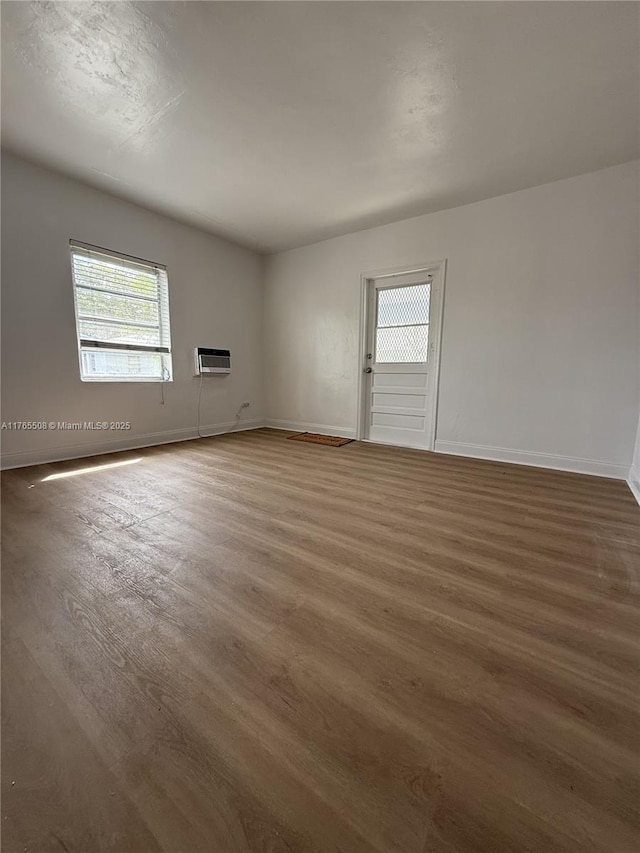 unfurnished room with a wall mounted air conditioner, baseboards, and wood finished floors
