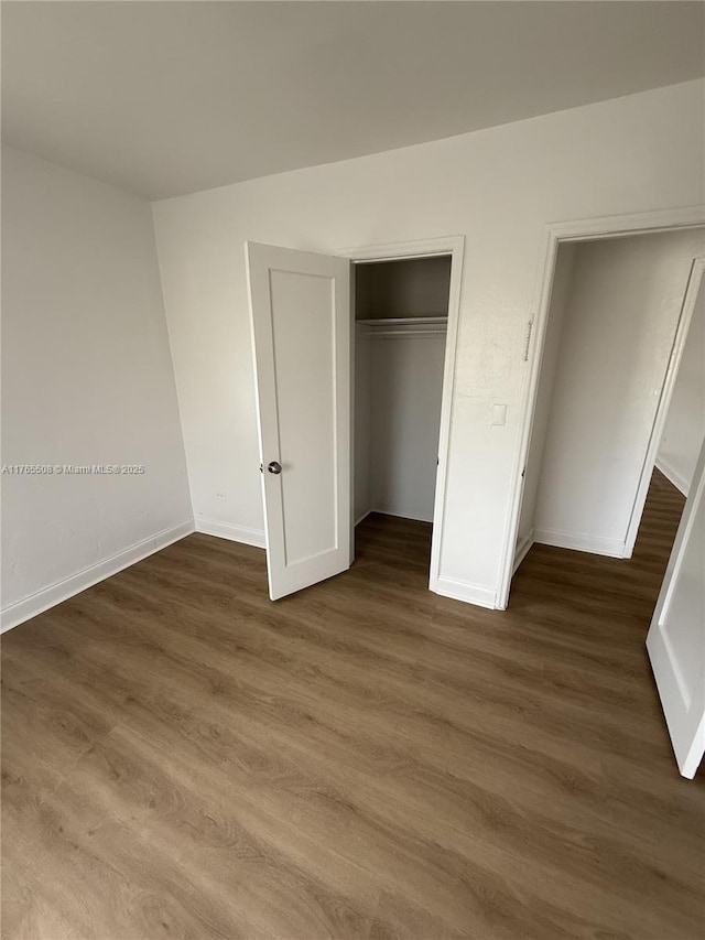 unfurnished bedroom with dark wood-type flooring, baseboards, and a closet