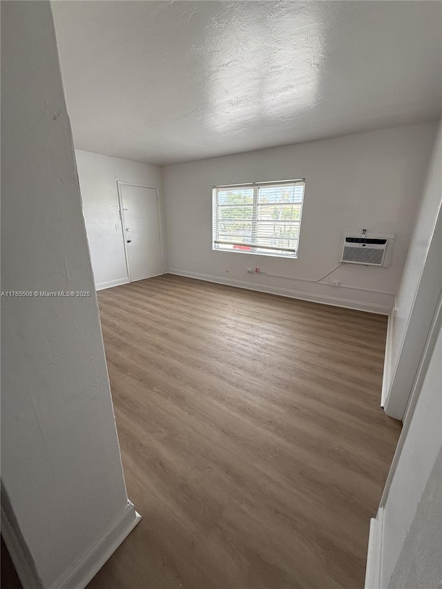 unfurnished room featuring baseboards, a wall unit AC, wood finished floors, and a textured ceiling
