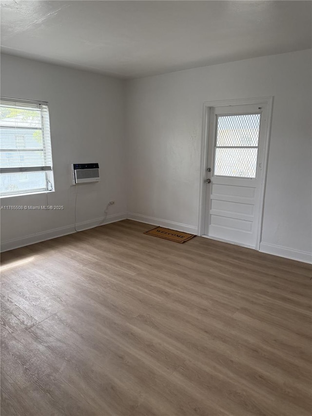 empty room featuring baseboards, wood finished floors, and an AC wall unit