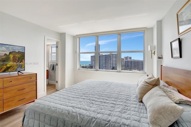 bedroom featuring multiple windows, light wood-style floors, and a view of city