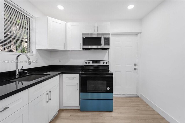 2911 NW 30th St, Miami, FL 33142 - kitchen with a sink, white cabinets, electric stove, stainless steel microwave, and light wood-type flooring