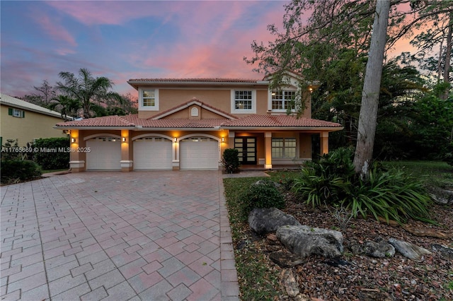 mediterranean / spanish house with stucco siding, a tile roof, decorative driveway, a porch, and a garage