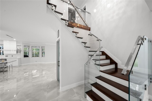 staircase with a high ceiling, baseboards, and marble finish floor