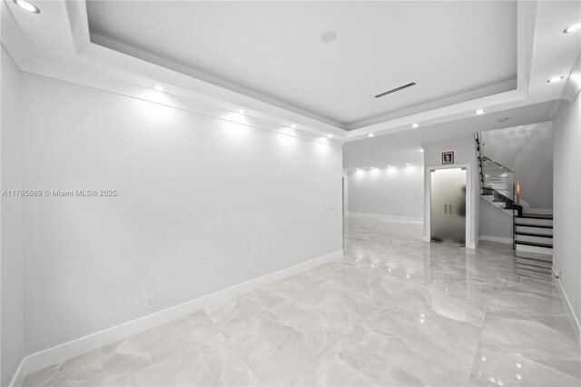 empty room with stairs, a raised ceiling, recessed lighting, and baseboards