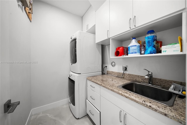washroom with cabinet space, stacked washer and clothes dryer, baseboards, and a sink
