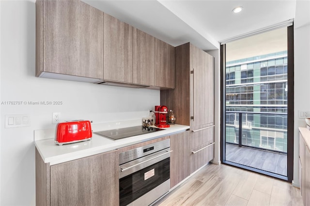 kitchen featuring oven, light countertops, floor to ceiling windows, black electric cooktop, and modern cabinets