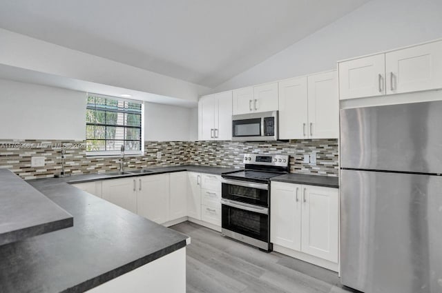 kitchen with white cabinetry, lofted ceiling, a sink, dark countertops, and appliances with stainless steel finishes