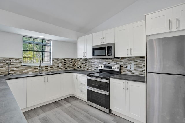 kitchen with decorative backsplash, appliances with stainless steel finishes, white cabinetry, a sink, and vaulted ceiling